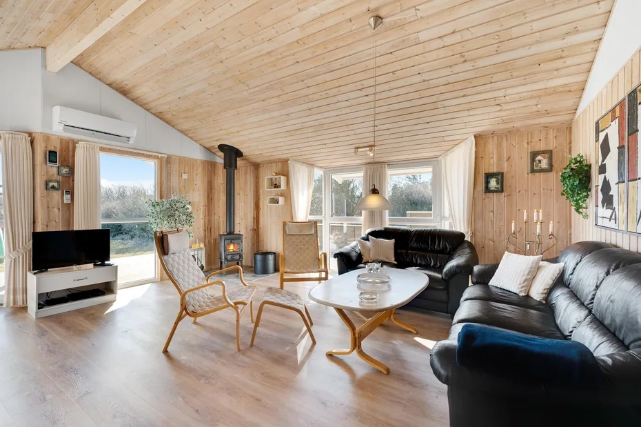 Una sala de estar revestida de madera, con asientos, un televisor y grandes ventanas.