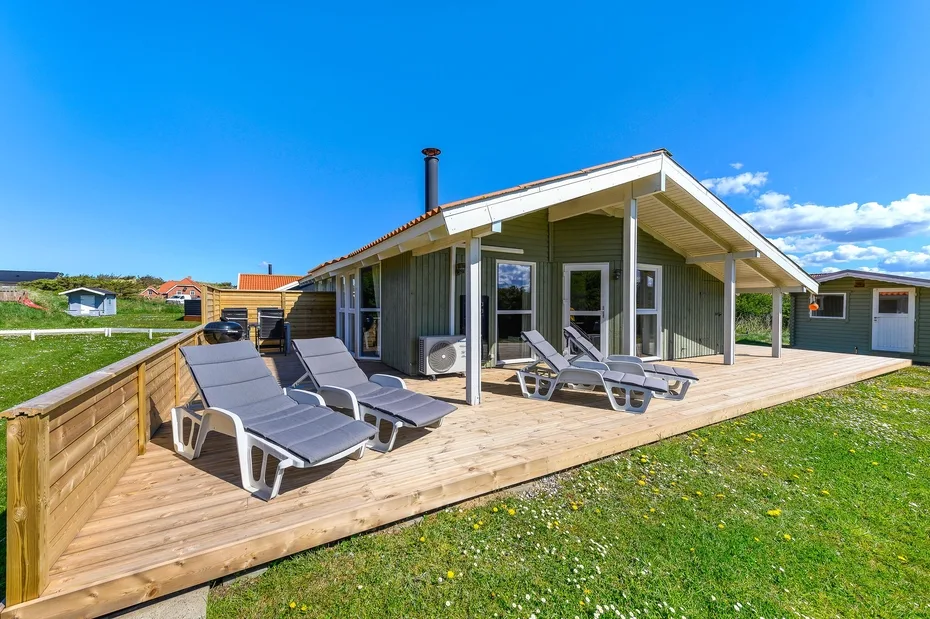 Una casa moderna da a una terraza de madera con asientos al aire libre.