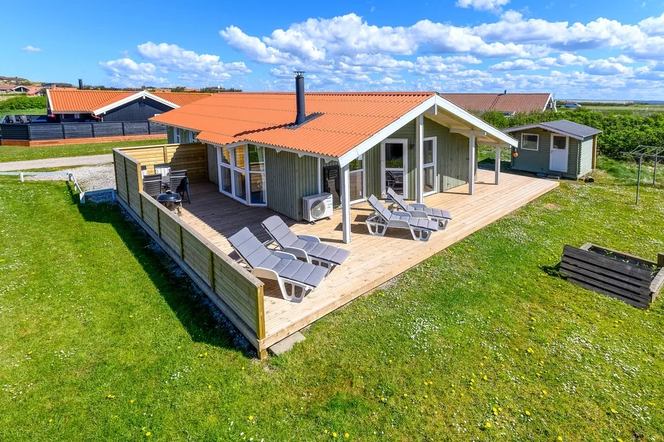 Una casa moderna con una terraza de madera y sillones de exterior.