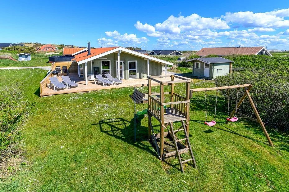 Una casa con una terraza de madera y un patio de césped con columpios.