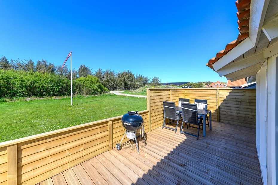 Una terraza de madera con asientos da a un jardín con césped.