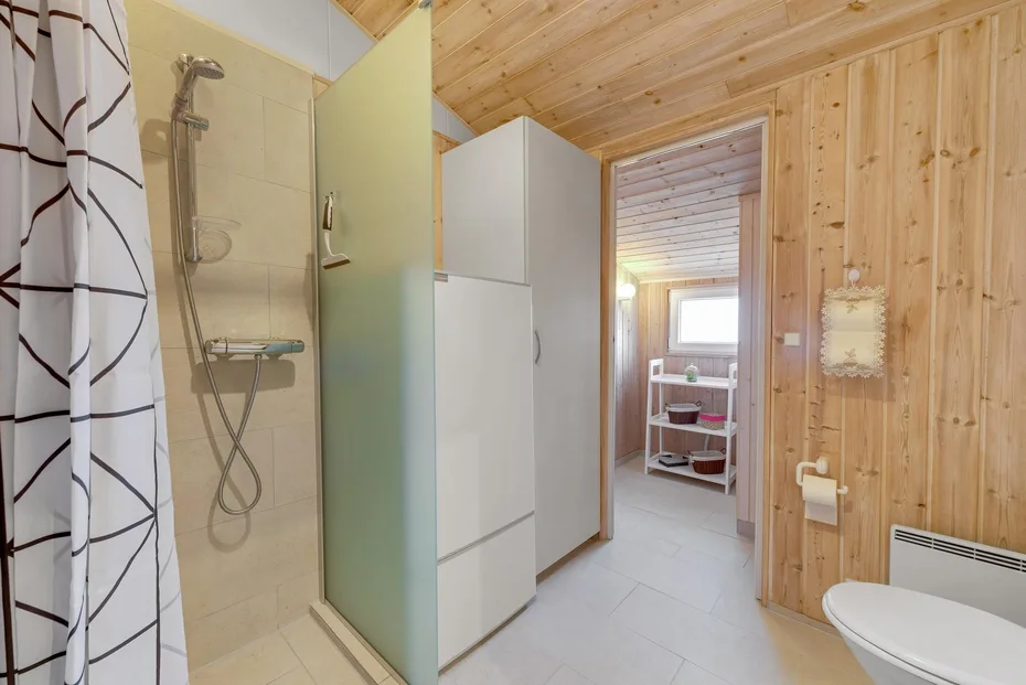 Un baño con ducha, inodoro y un armario blanco.