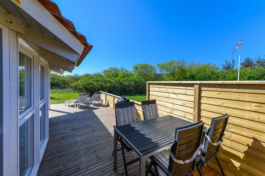 Una terraza exterior tiene una mesa de comedor y asientos junto a una cerca de madera.