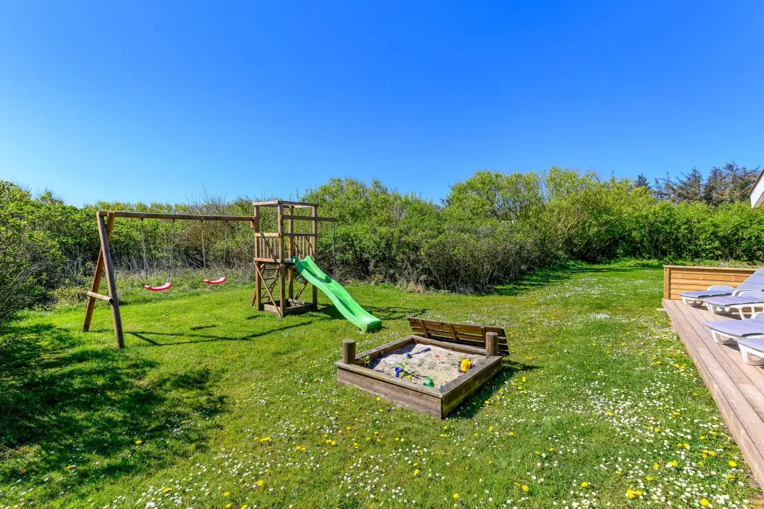 Un patio con césped tiene una estructura de juego de madera con un tobogán verde y un arenero.