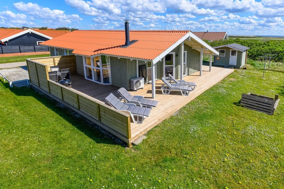 Una casa moderna con una amplia terraza de madera y asientos al aire libre.