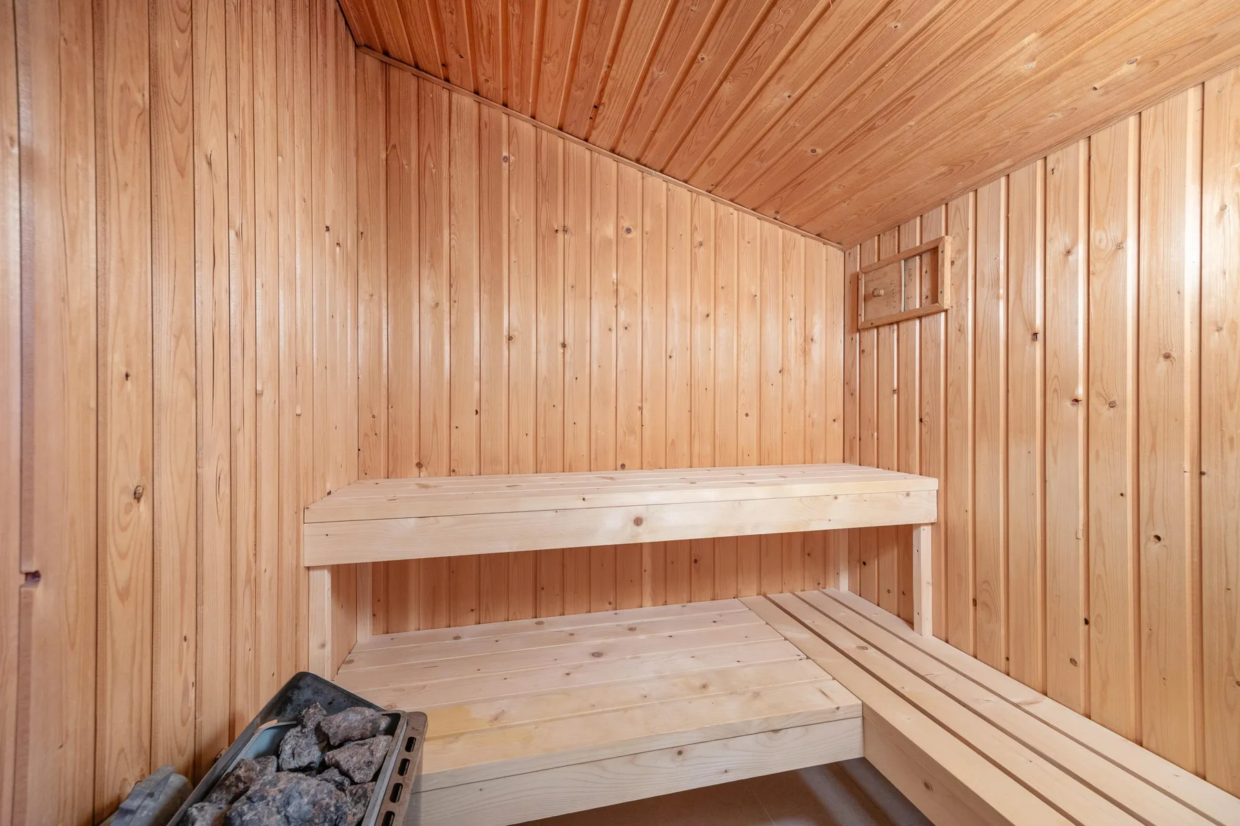 Una sauna revestida de madera con asientos escalonados y un calentador.