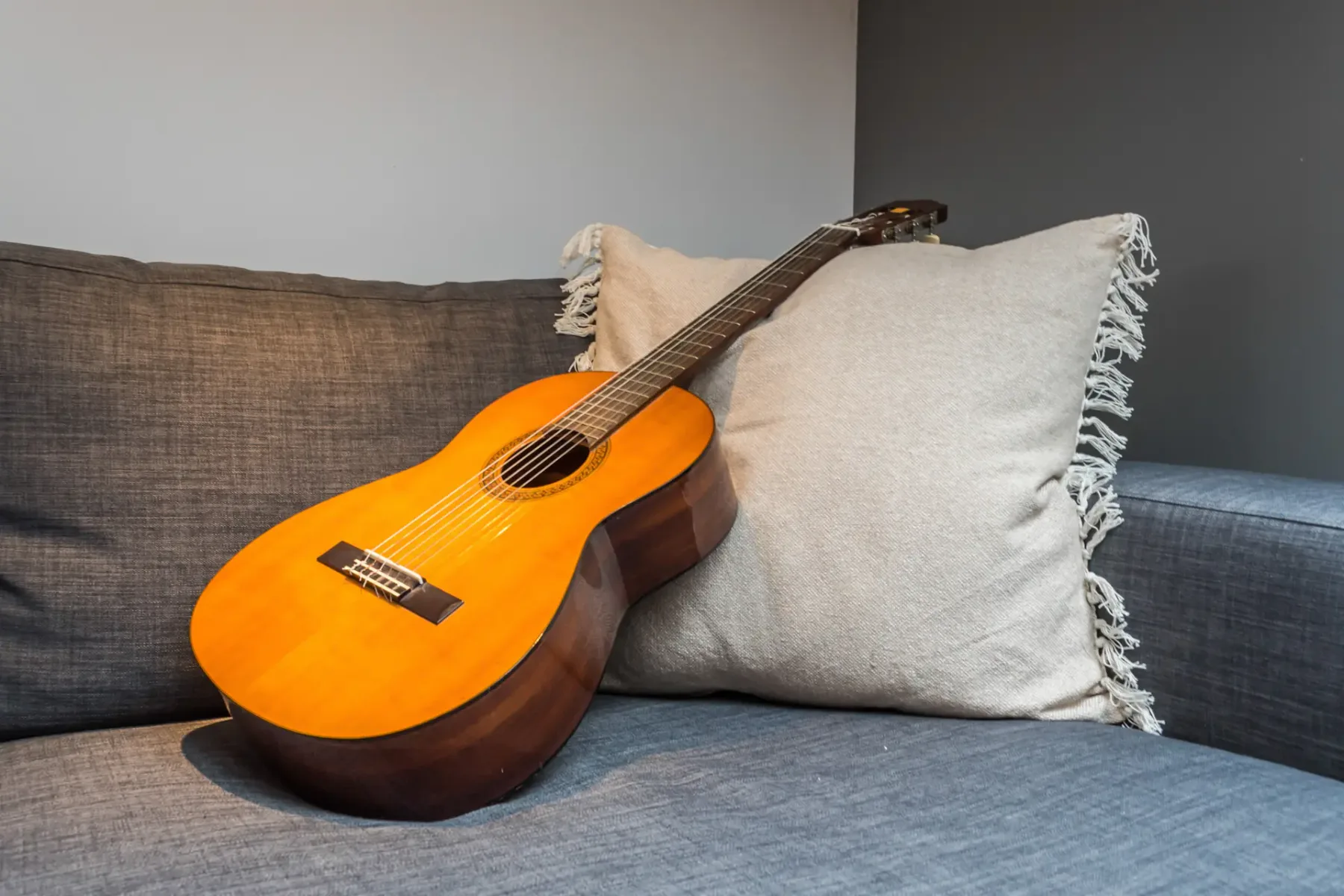 Una guitarra descansa sobre un sofá gris junto a un cojín claro.