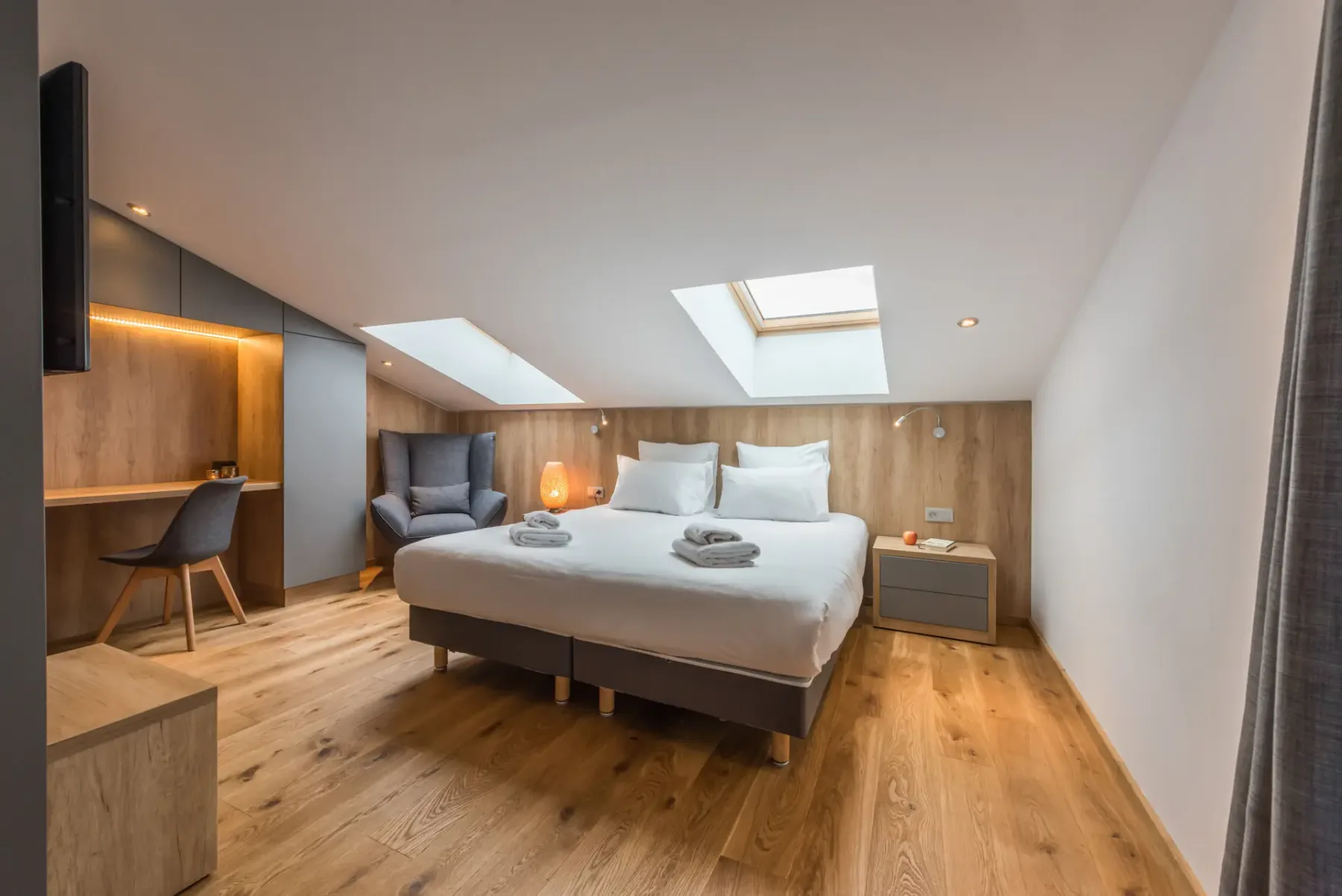 Dormitorio con una cama, mesita de noche, escritorio y techo inclinado con claraboyas.