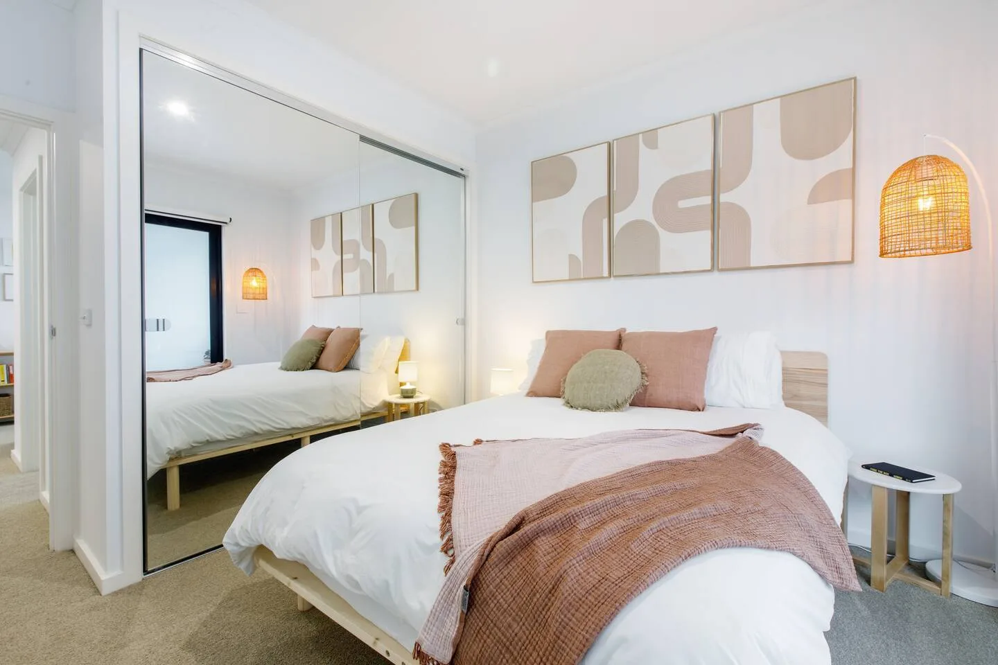 Un dormitorio luminoso presenta una cama bien arreglada, puertas de armario espejadas y arte mural.