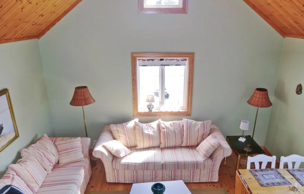 Una sala de estar con asientos a rayas, lámparas y una ventana bajo un techo inclinado.