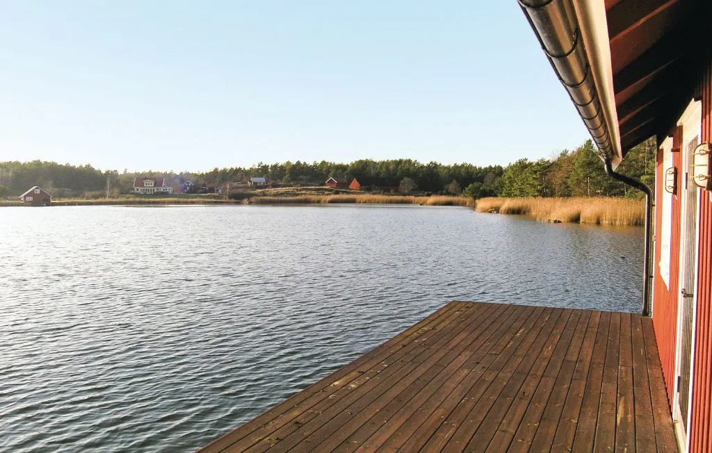 Una terraza de madera junto a un lago, con un edificio rojo a un lado.