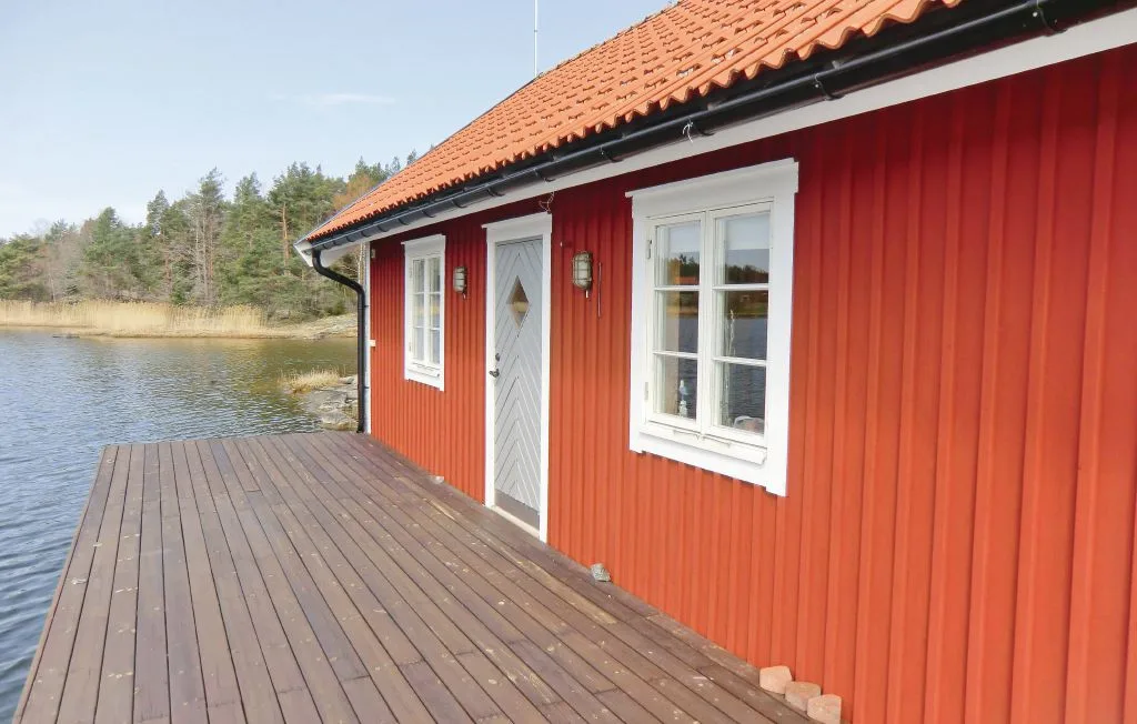 Una cabaña roja junto a un lago tiene una terraza de madera y ventanas con marcos blancos.