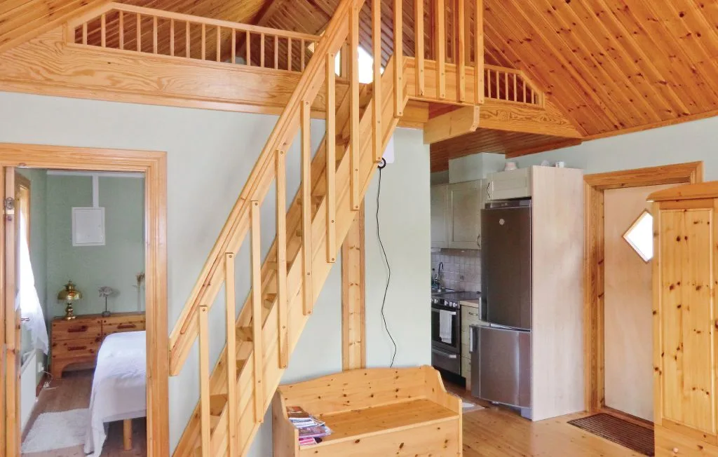 Una escalera de madera sube junto a una pequeña cocina en un interior luminoso.
