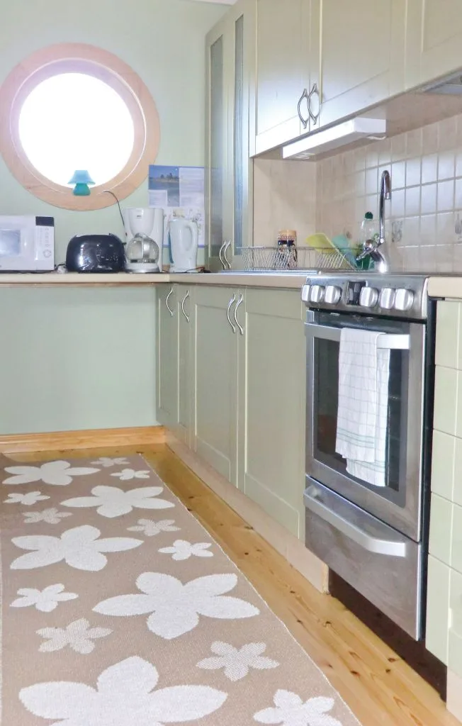 Una cocina compacta con gabinetes claros, una encimera y una alfombra floral.