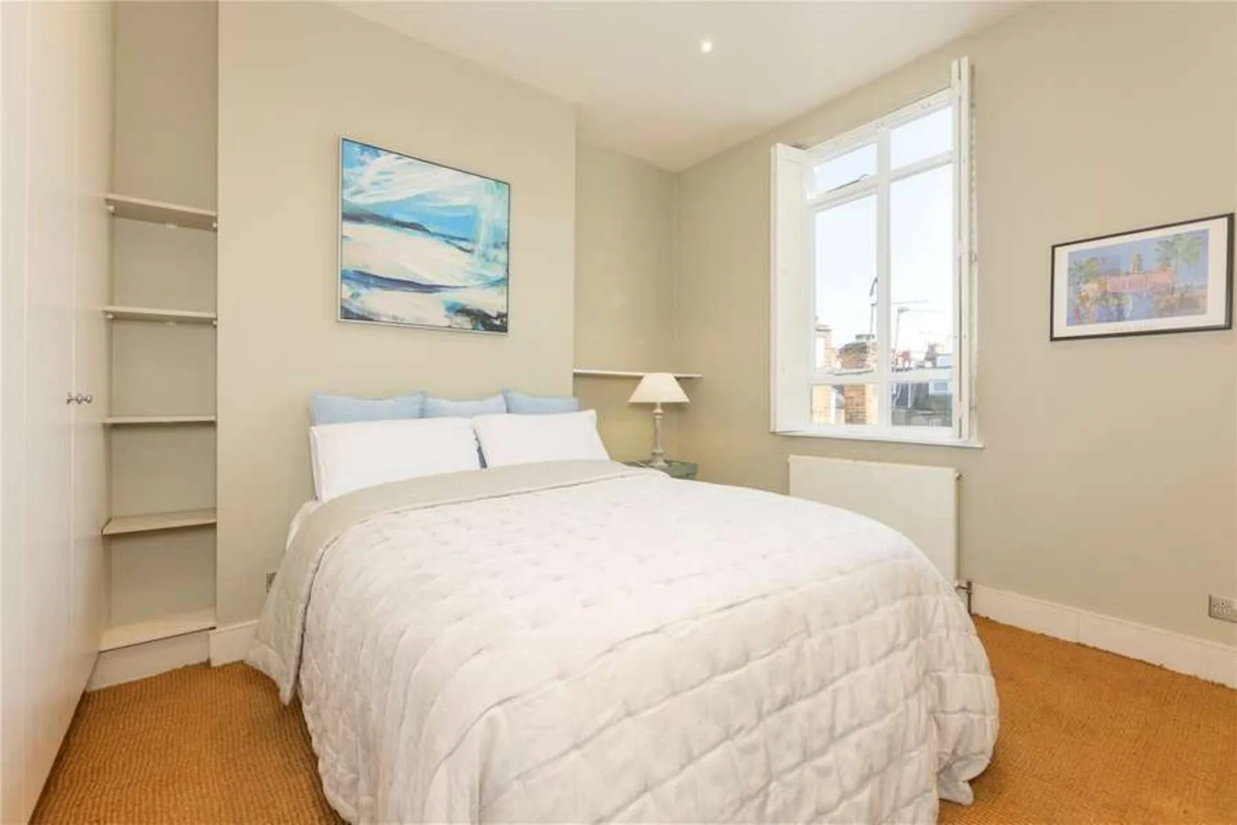 A bright bedroom with a bed, built-in shelves, and a large window.
