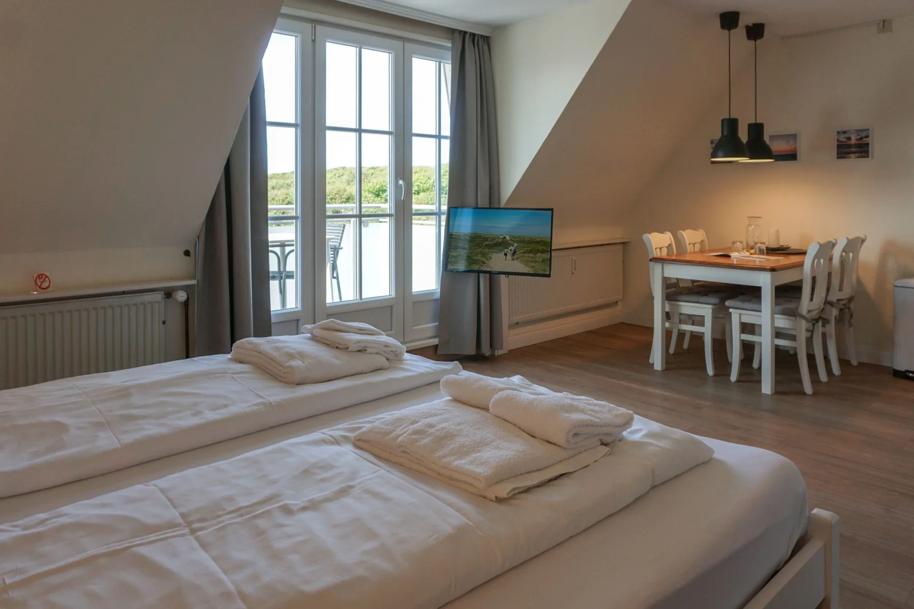 Un dormitorio abuhardillado luminoso con camas junto a ventanas altas y una mesa de comedor.
