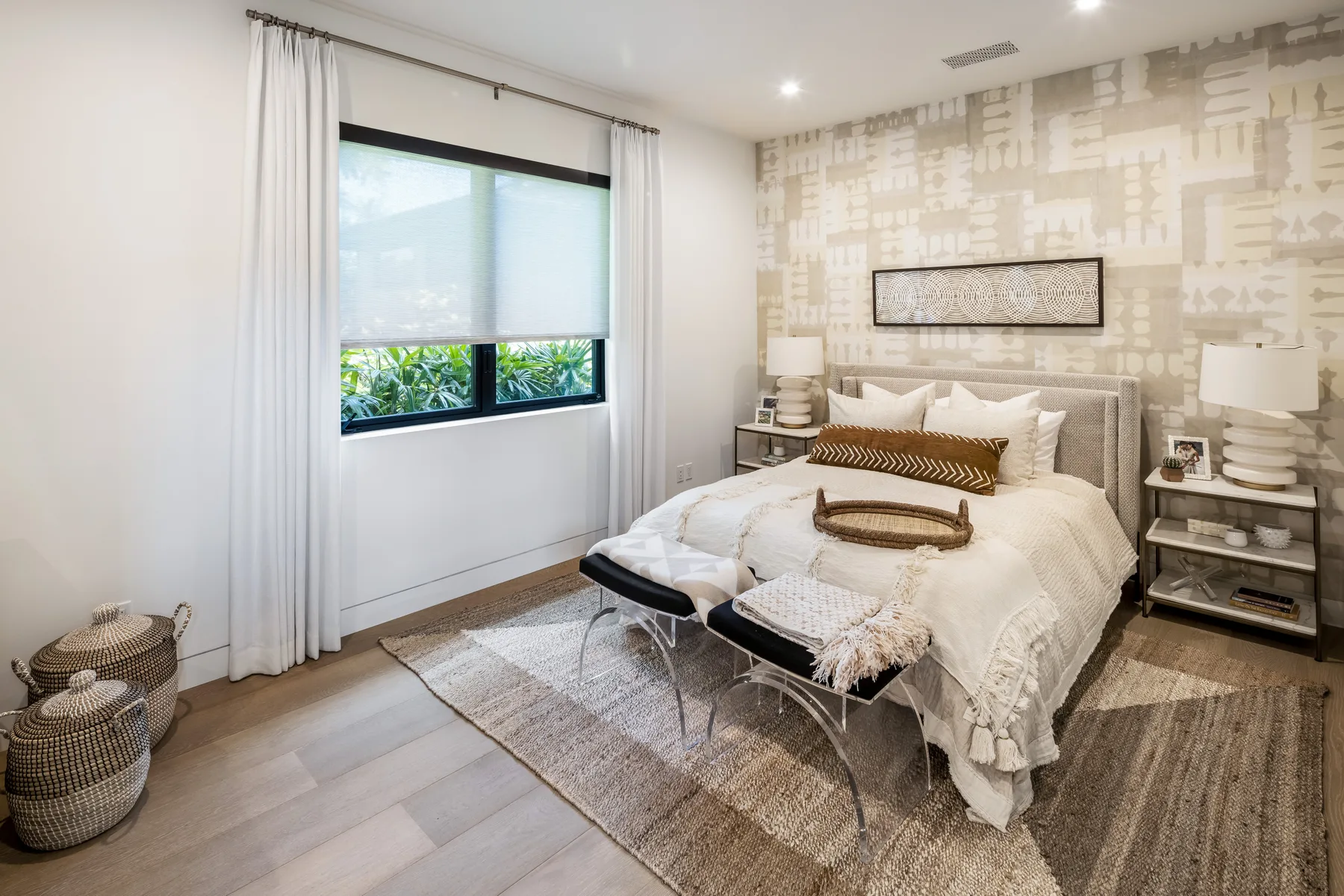 A bedroom with a neatly made bed, patterned accent wall, and large window.