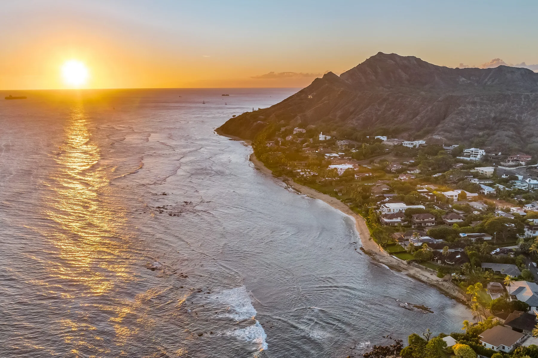 A coastal landscape at sunset, with ocean waves beside a mountainous shoreline.