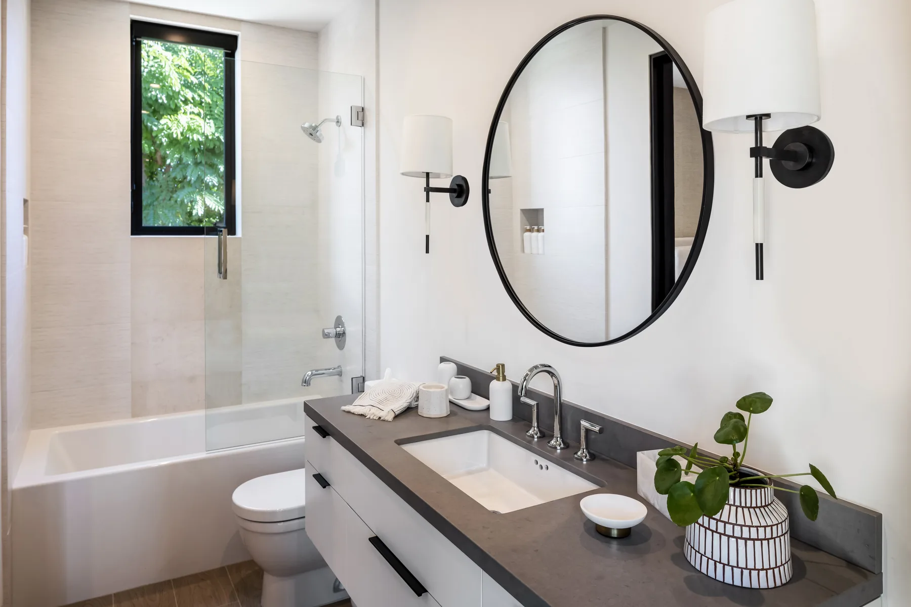 A bright bathroom with a bathtub, toilet, and vanity beneath a large mirror.