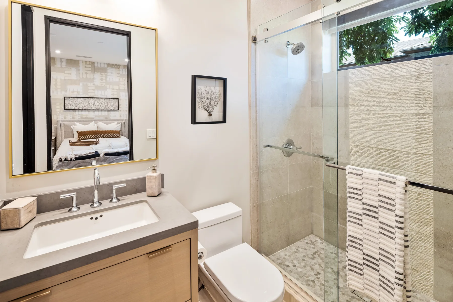 A bathroom with a sink, toilet, and glass shower beside a window.