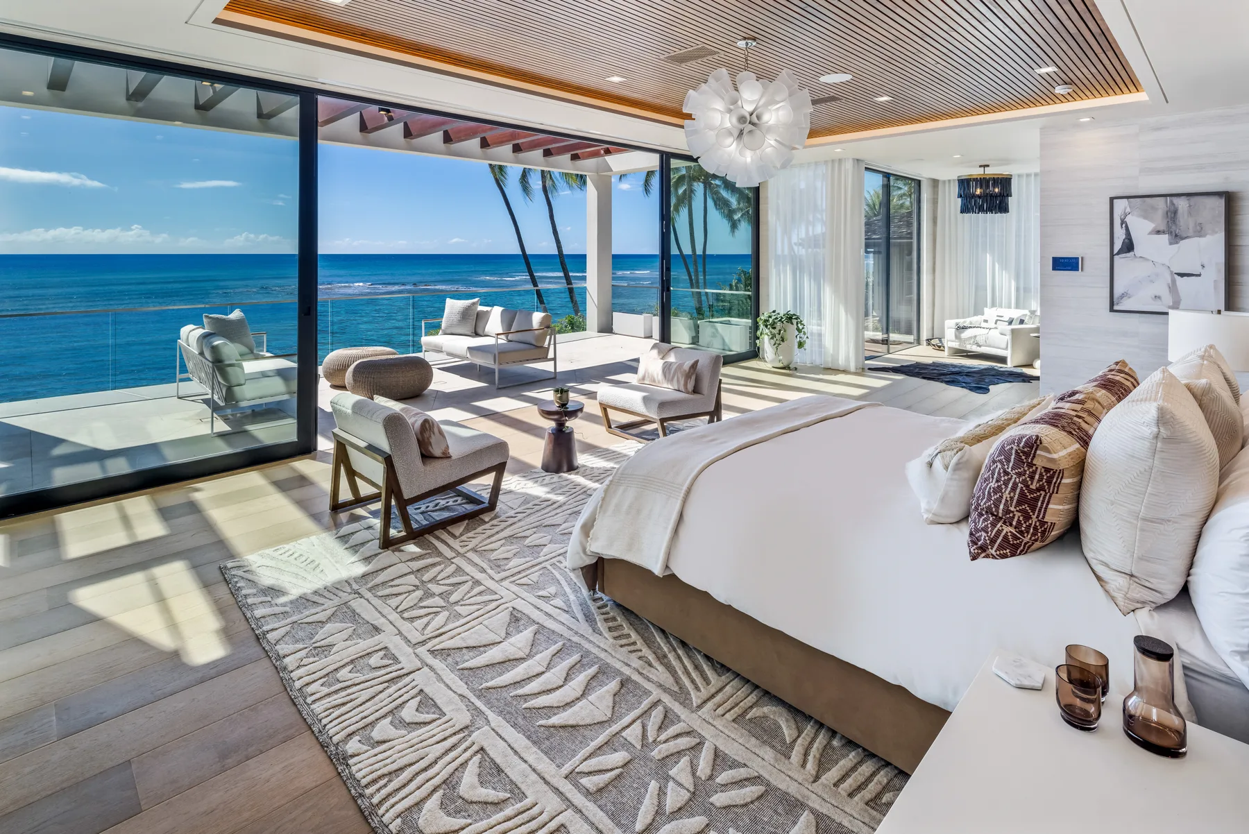 A bright bedroom opens onto an ocean view, with a bed and seating by the windows.