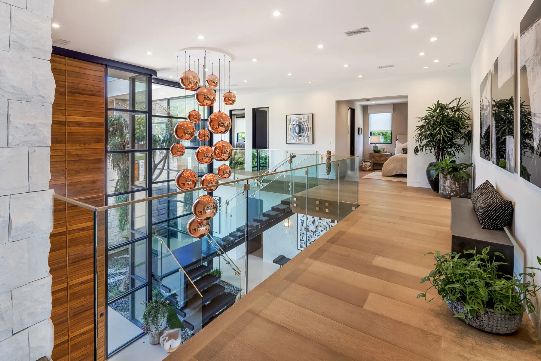 A bright upstairs hallway overlooks a staircase behind glass railings.