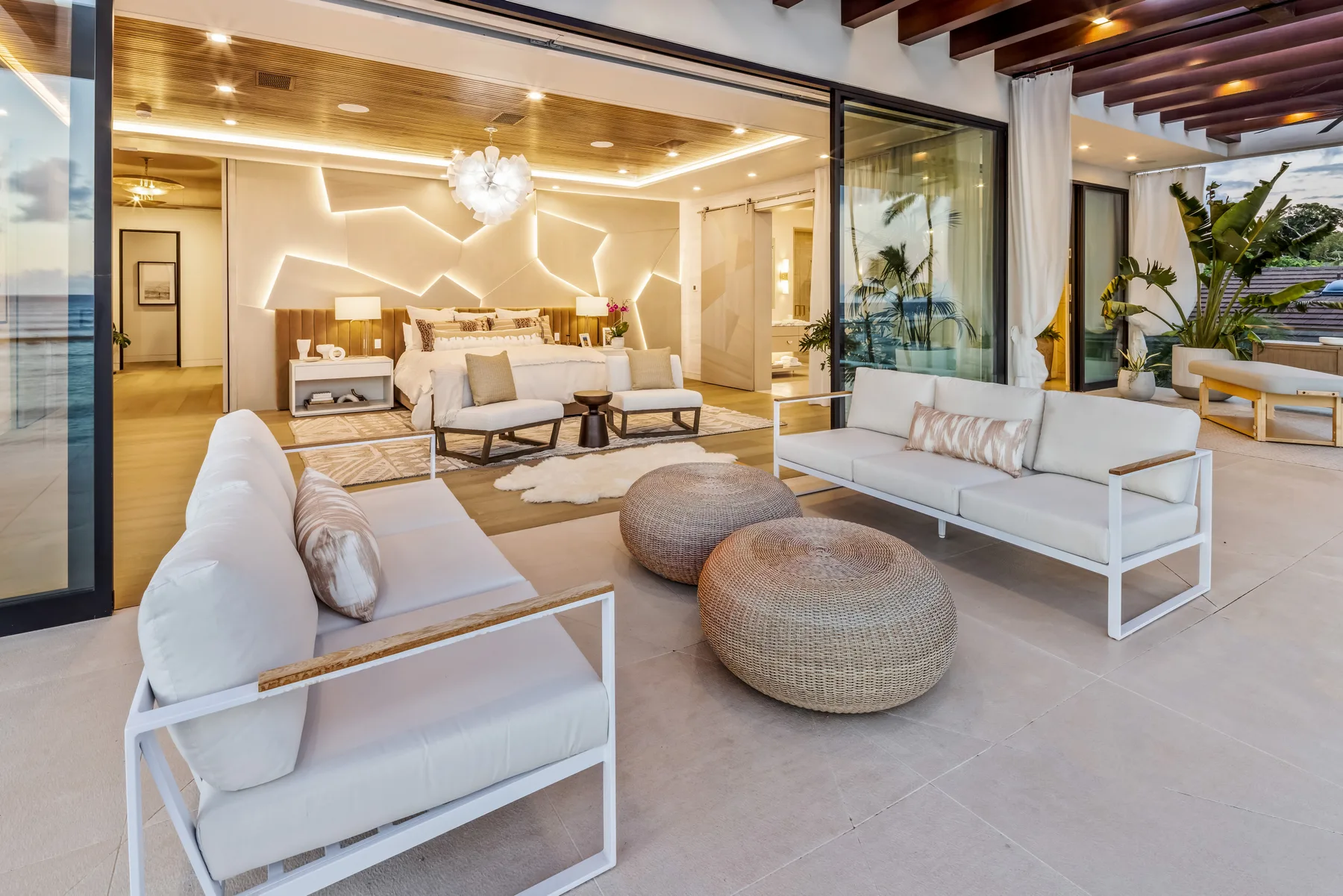 A bright living room opens onto a covered patio, with white seating and round ottomans.