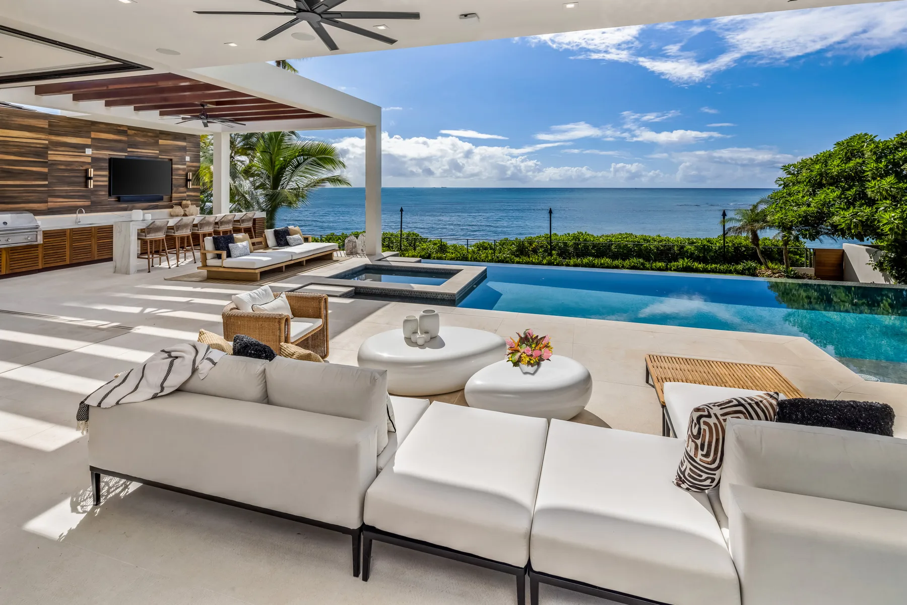 An outdoor lounge and pool overlook the ocean, with seating beneath a covered patio.