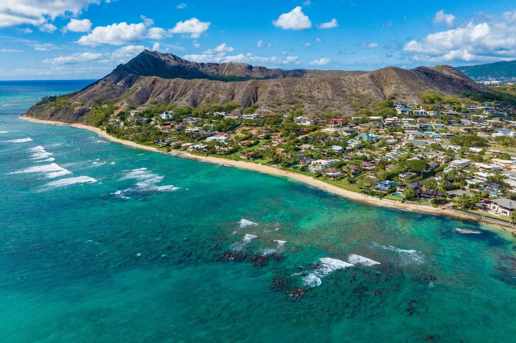 Aerial view of a coastal neighborhood between turquoise water and a mountain ridge.