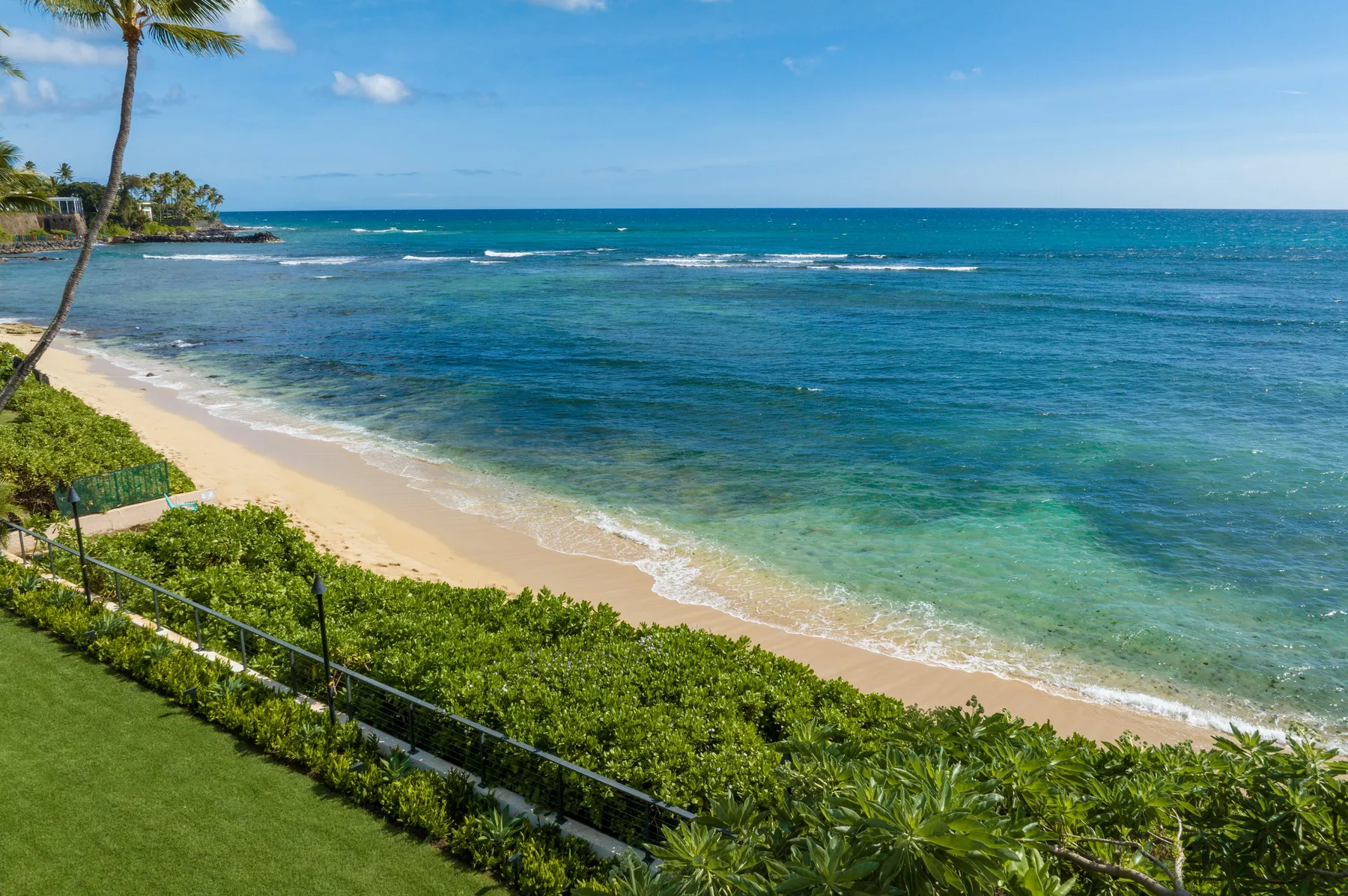 A sandy beach borders clear turquoise water beside green coastal vegetation.