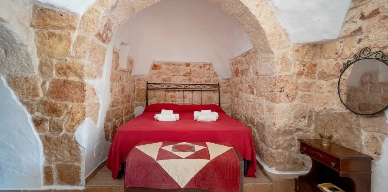 A bedroom with a red-covered bed beneath a stone arch.
