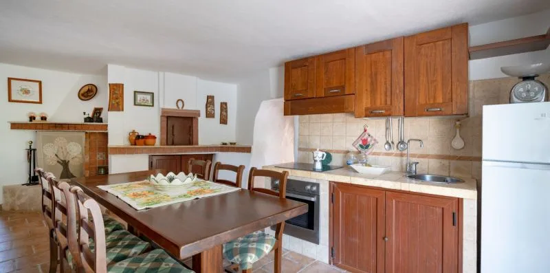 A dining area beside a kitchen, with a long table and wooden cabinets.