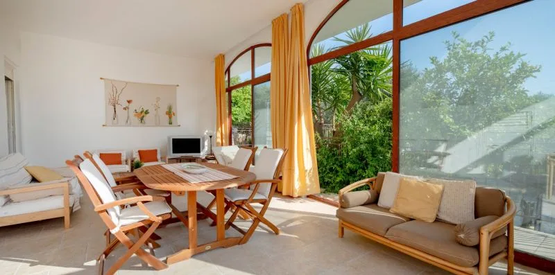 A bright living and dining area with a round table and large windows overlooking greenery.