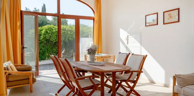 A dining area with a wooden table and chairs beside large glass doors.