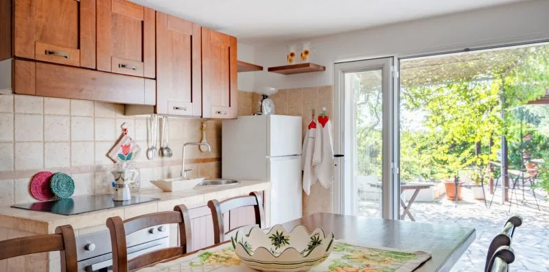 A kitchen with wooden cabinets and a dining table beside a glass door.