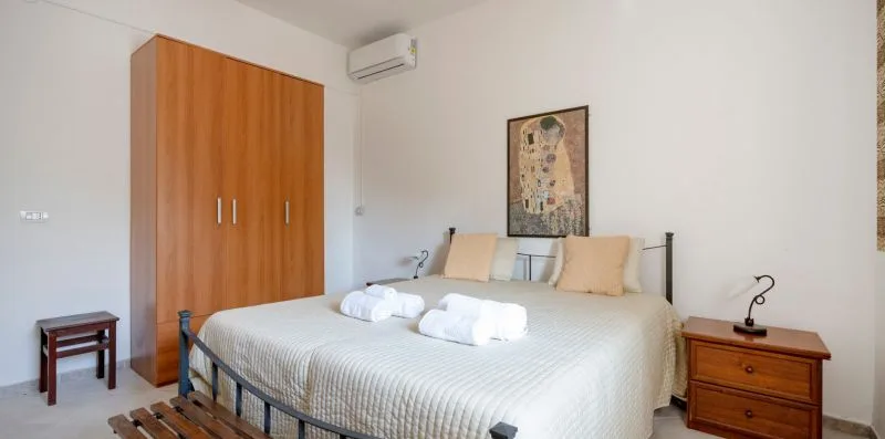 A bedroom with a neatly made bed, folded towels, and a wooden wardrobe.
