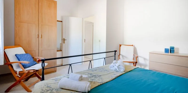 A bedroom with a bed, folded towels, and a wooden wardrobe.