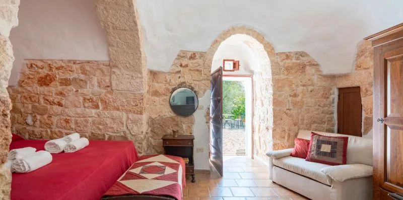 A rustic living room with a red bed, seating, and an arched doorway.