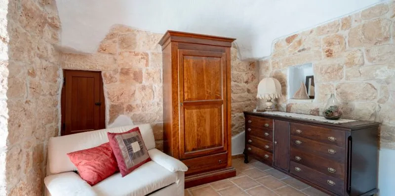 A stone-walled room with a white sofa, wooden cabinet, and dresser.