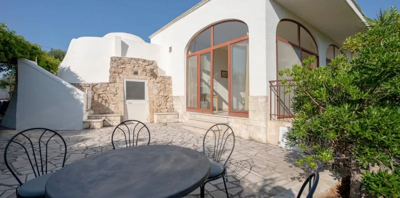 A sunlit stone patio with outdoor seating beside a white building.