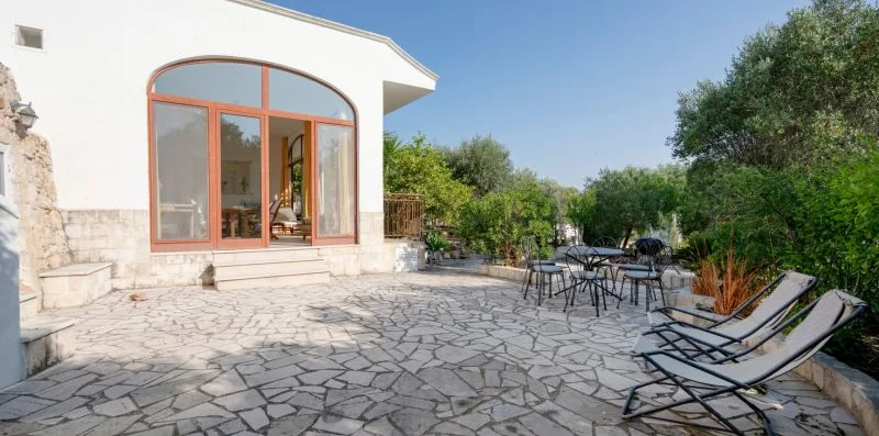 A stone-paved patio has outdoor seating beside a building with arched glass doors.