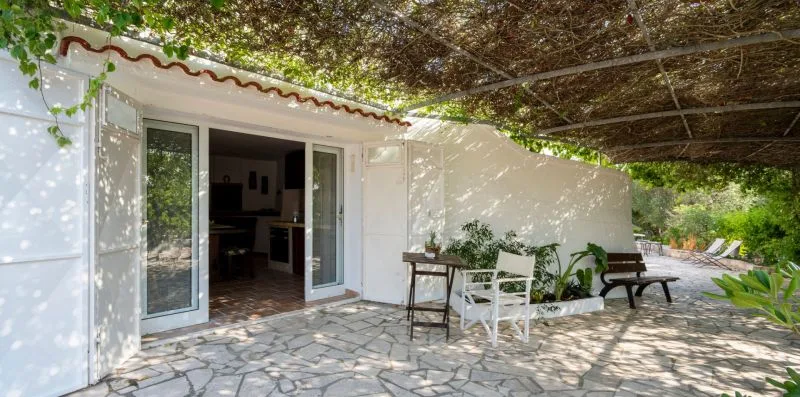 A shaded outdoor patio with white seating beside an open doorway.