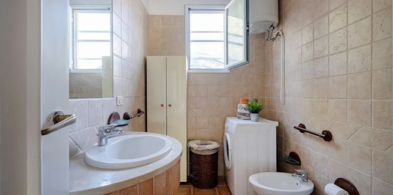 A tiled bathroom with a sink, washing machine, and open windows.