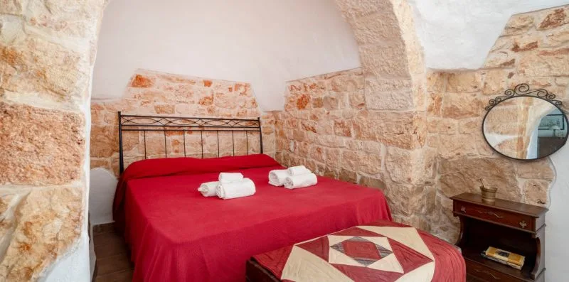 A bedroom with a red-covered bed beneath a stone arch.