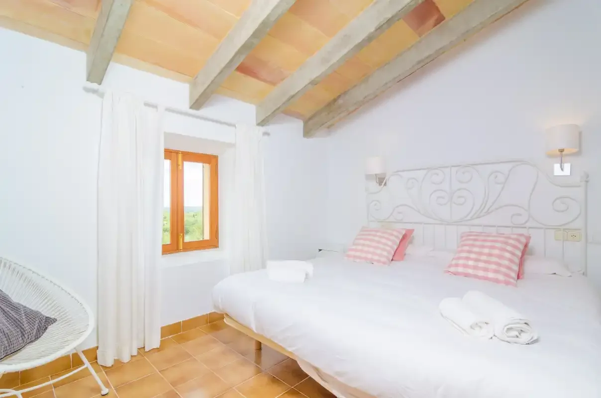 A bright bedroom with a large bed, decorative metal headboard, and wood-beamed ceiling.