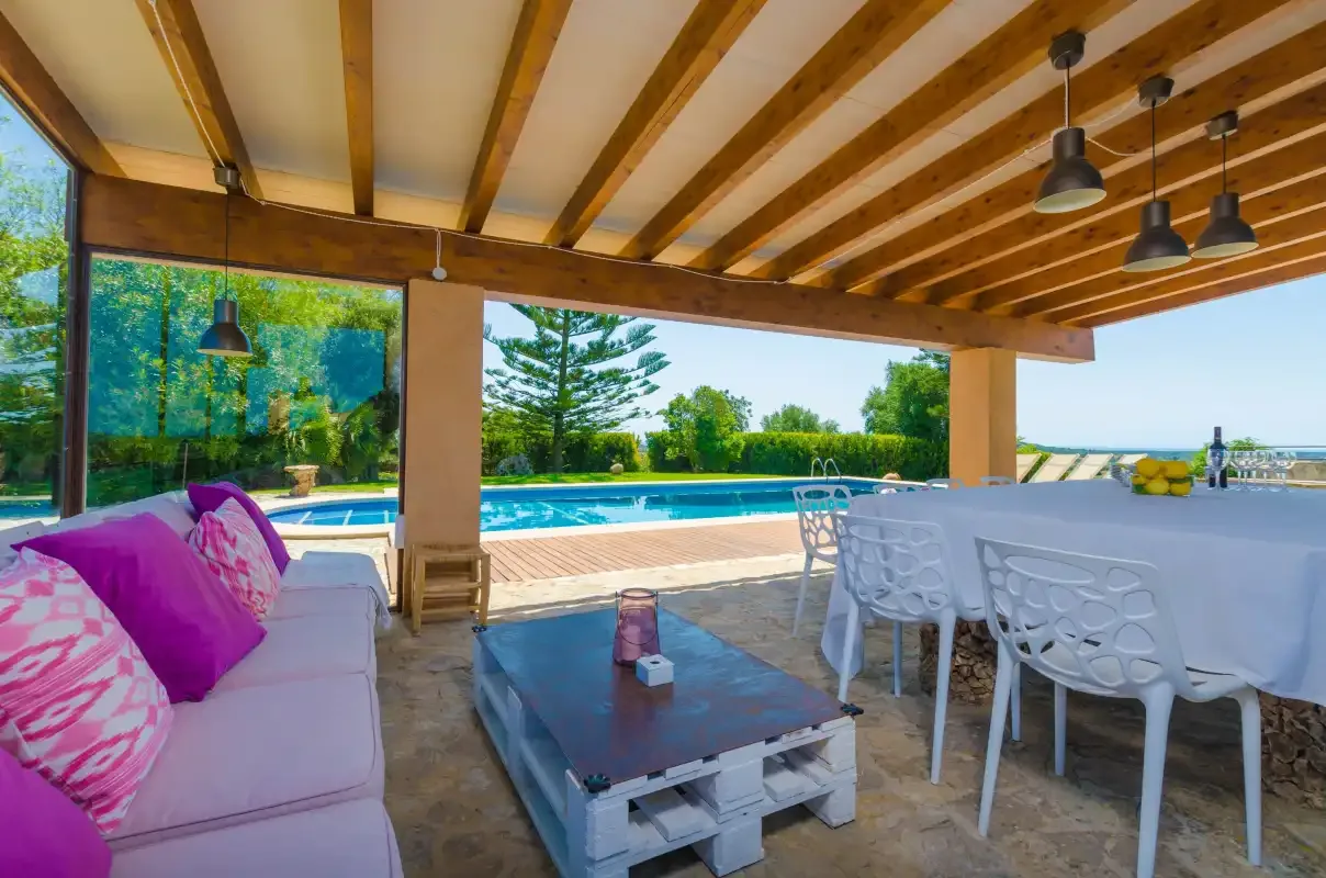 A covered outdoor dining and seating area overlooks a swimming pool.