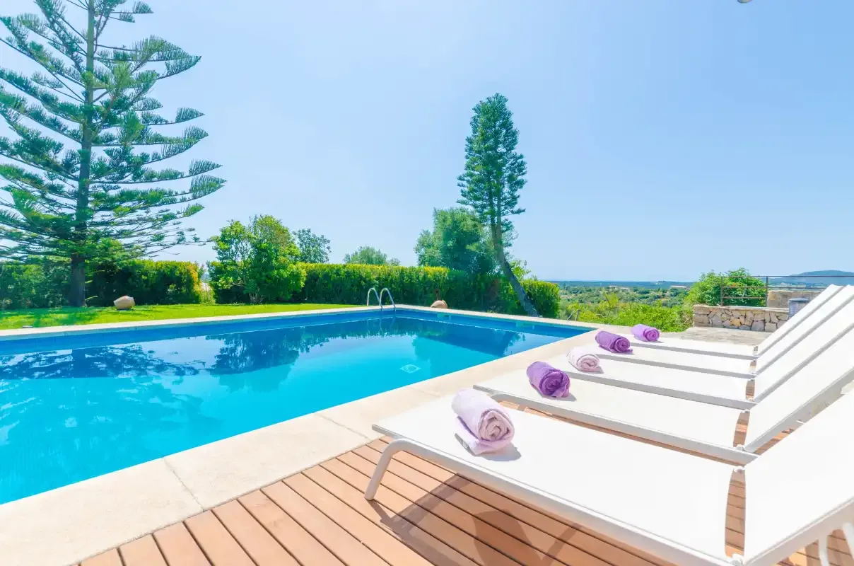 An outdoor swimming pool beside white loungers and a wooden deck.