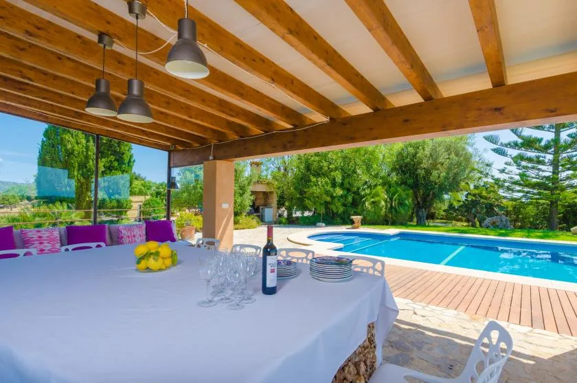 A shaded outdoor dining area overlooks a swimming pool and garden.