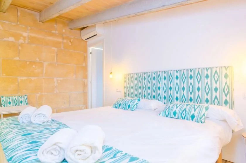 A bedroom with a large bed dressed in white linens and patterned teal accents.