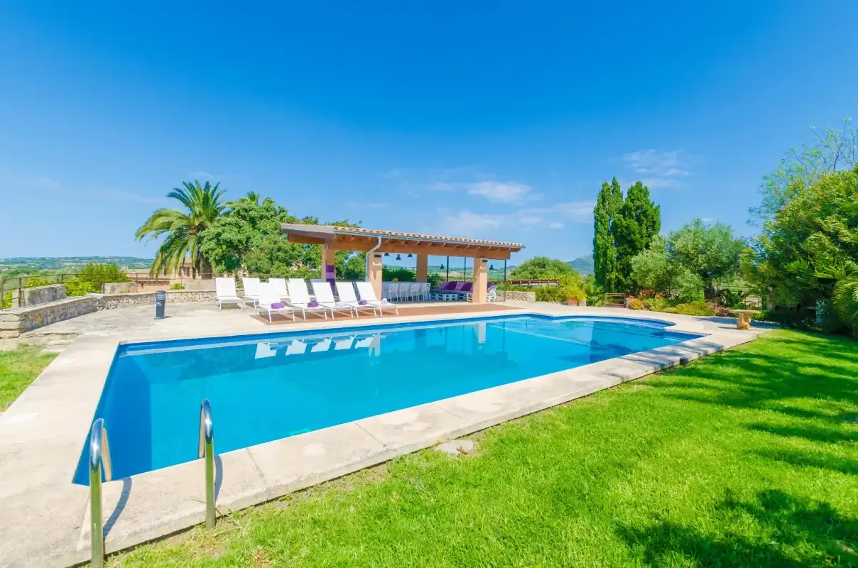 An outdoor swimming pool is surrounded by a paved deck and green lawn.